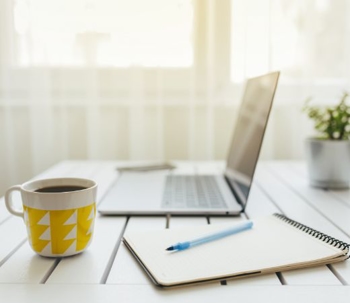 Laptop, coffee mug, and notepad on top of a desk.
